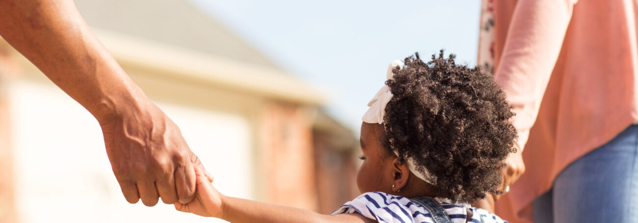 Side view of toddler girl holding her parents' hands as they walk outside