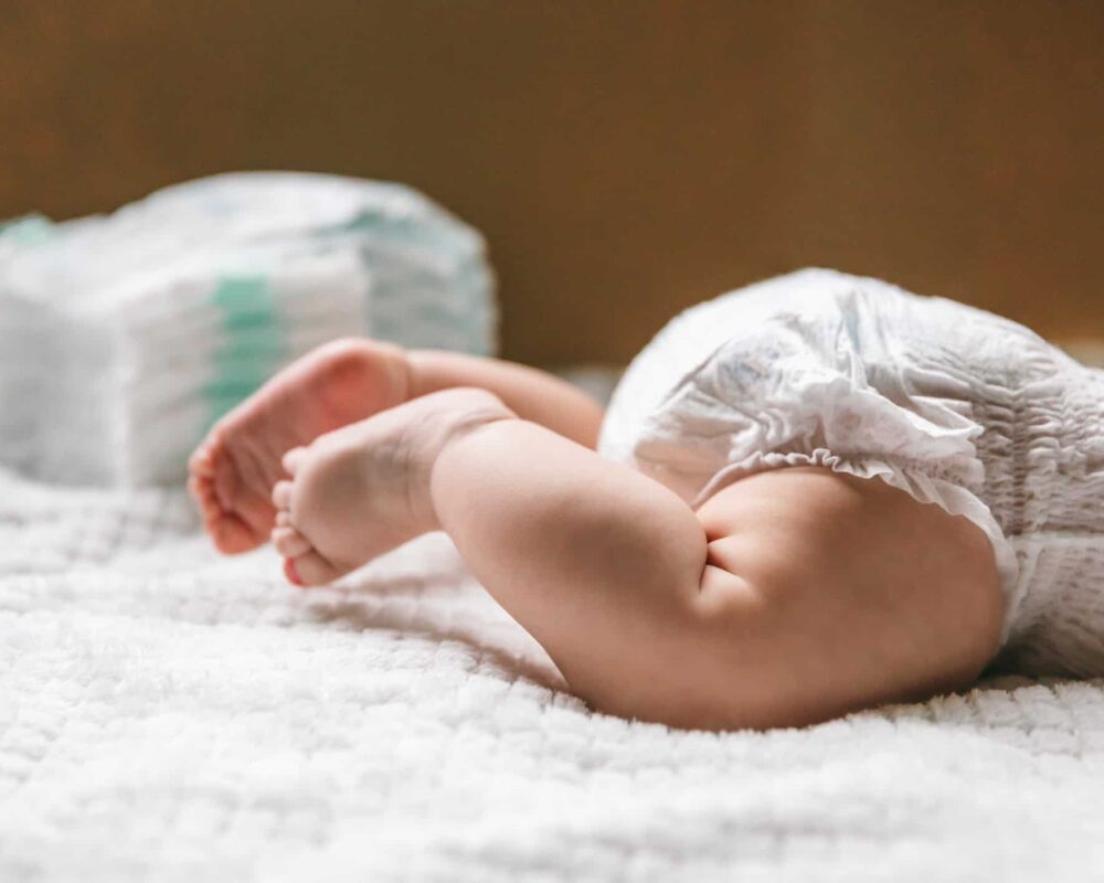 A baby wearing a diaper lies on a changing pad with a stack of diapers in the background