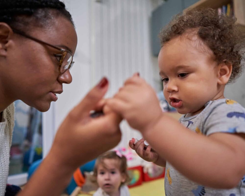 Young mother holds toddler son's fingers as he tries to take steps