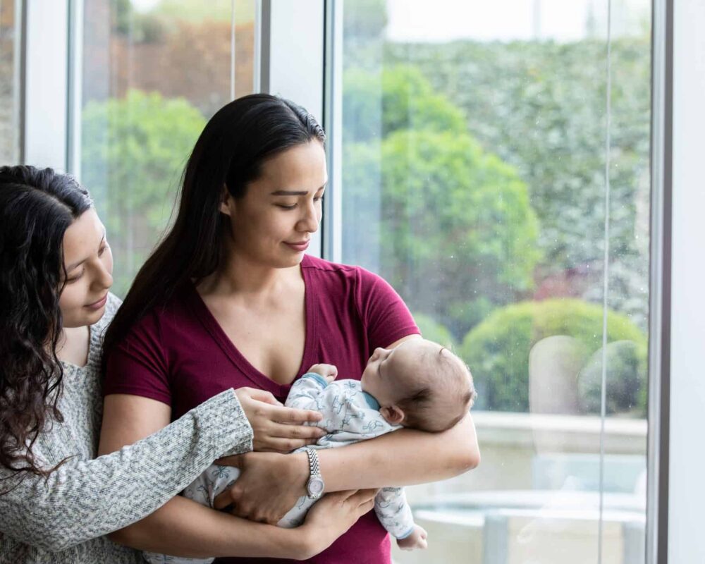 Mom cradles newborn while home visitor shows her proper way to hold them