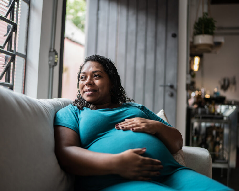 Maternal figure cradles her baby bump while looking out the window