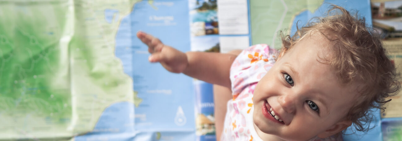 Baby girl sits on giant floor map and smiles up at the camera