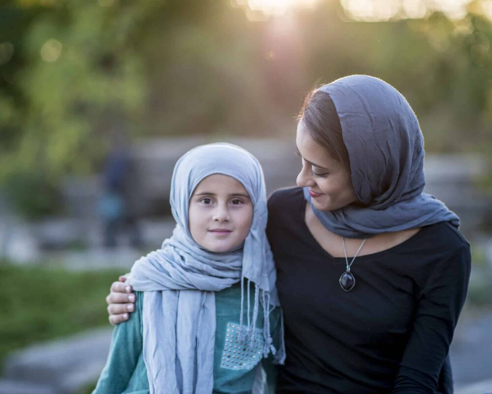 Woman puts her arm around her daughter while sitting on a park bench