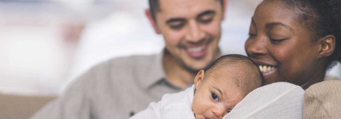 Multiracial family snuggles with their newborn while sitting on the couch