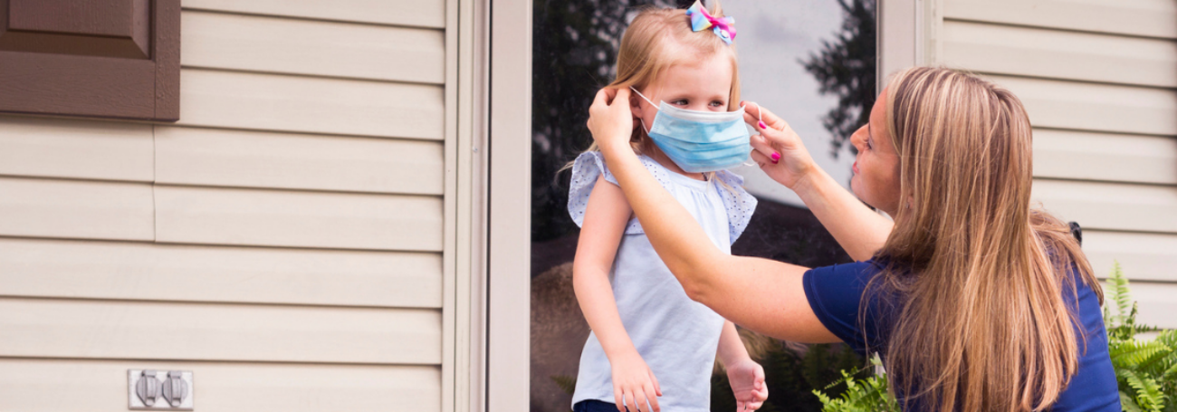 Mom puts mask on a young girl before entering a house