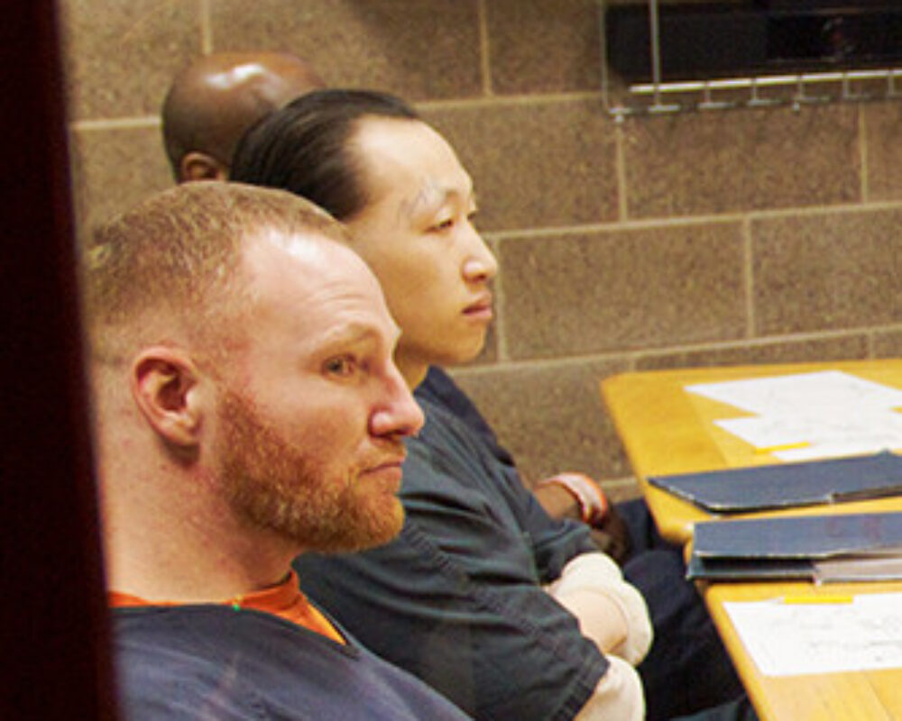 Three men sit around a large table listening to others speak