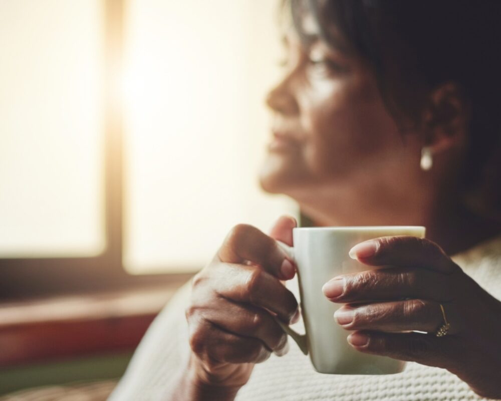 Woman holds mug of tea in hand while staring out the window
