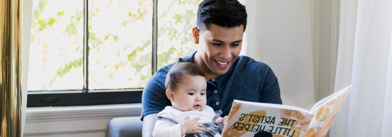 Father holds his baby daughter on his lap while reading her a book