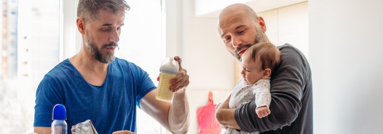 Fathers make formula and comfort their crying baby in their kitchen