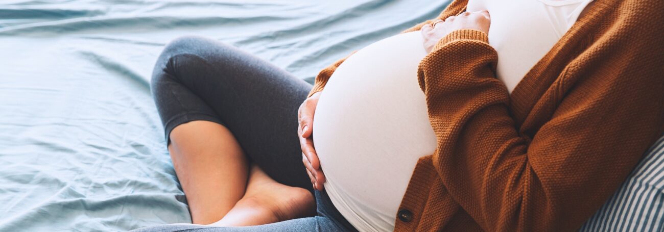 Close-up of pregnant woman wearing an orange sweater and holding her belly