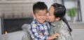 Mother in military clothing kisses her son's cheek as he smiles