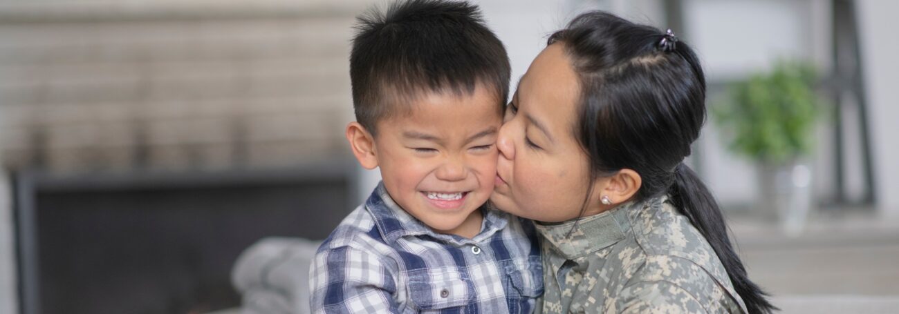 Mother in military clothing kisses her son's cheek as he smiles