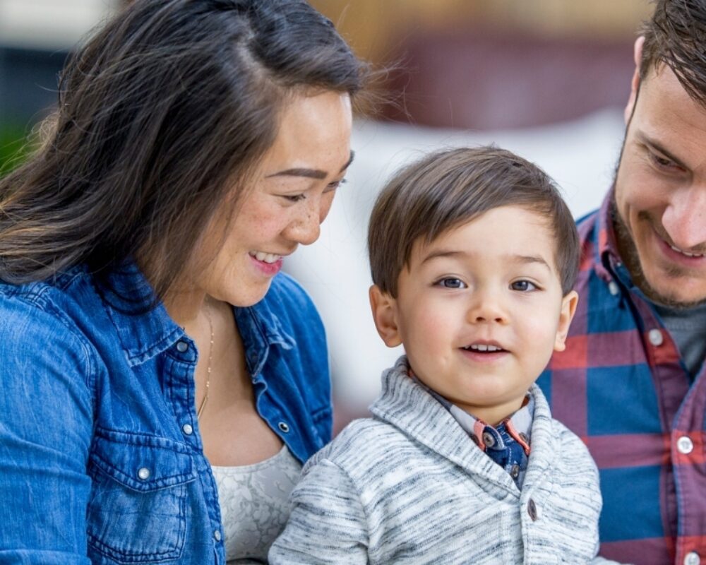 Mixed-race family poses for photo as parents smile at boy staring at the camera