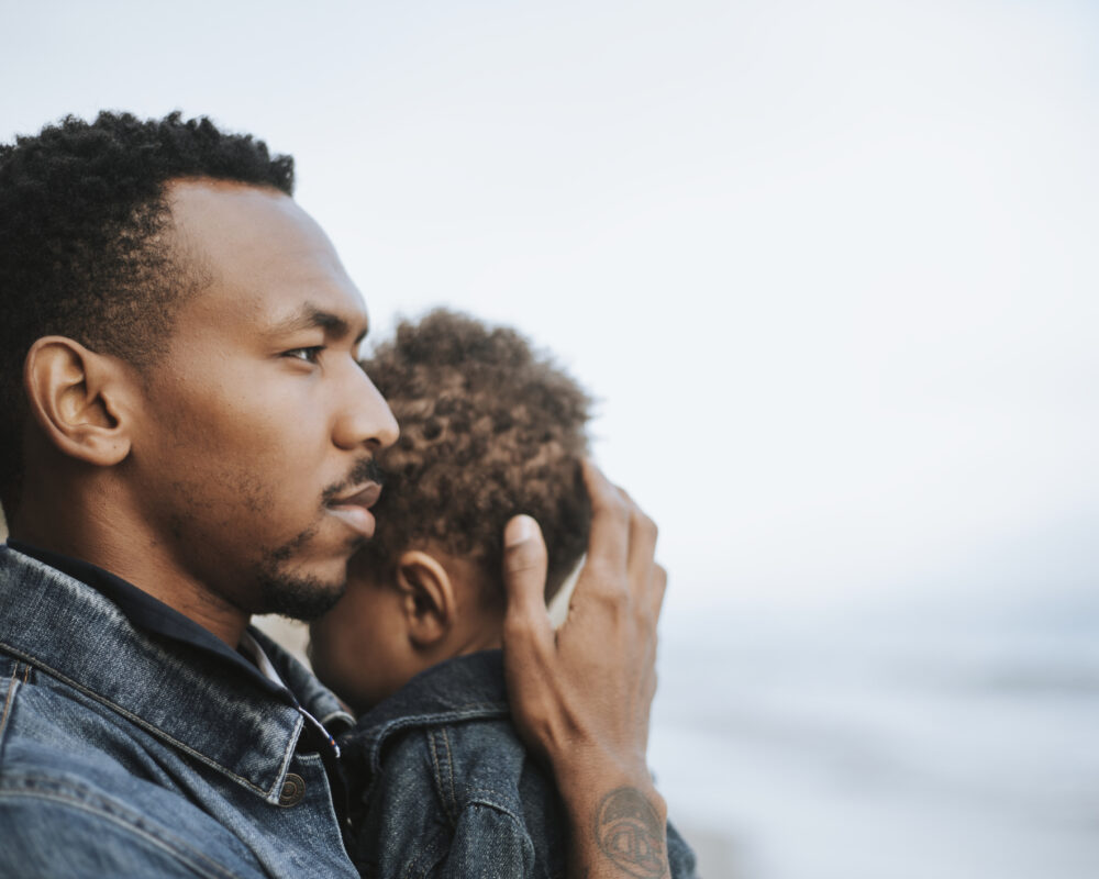 A father cradles his toddler against him while staring into the distance