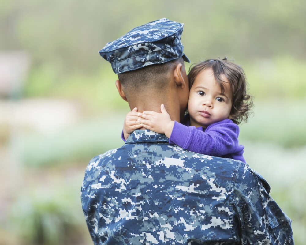 Toddler girl hugs her father wearing a military uniform