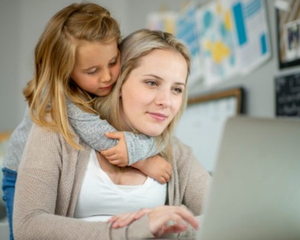 Daughter wraps arm around mom while she is searching on computer