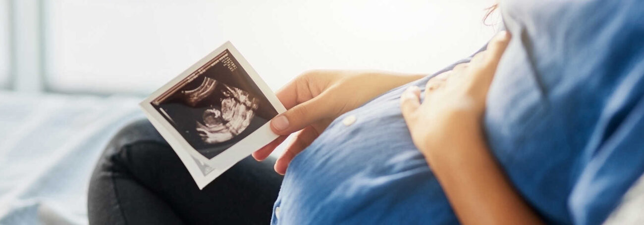 pregnant person cradling bump and looking at ultrasounds photo
